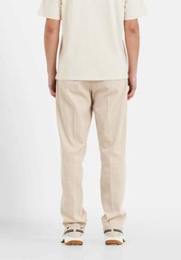 Beige broeken met een recht model en subtiele plooien, gecombineerd met een crèmekleurig t-shirt en lichtgekleurde sneakers.