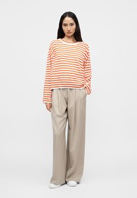 Haut à manches longues rayé orange et blanc, associé à un pantalon large beige. Des baskets blanches complètent la tenue. Texture de tissu lisse.