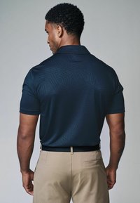 Marineblå polo T-shirt med geometrisk tekstur, kortærmede og krave, som er parret med khaki bukser. Fokuser på design og materialedetaljer.