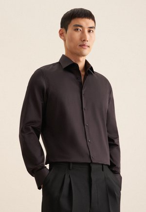 Schwarzes Langarmshirt mit klassischem Kragen, knopfbarem Vorderteil und glattem Stoff. Kombiniert mit maßgeschneiderten schwarzen Hosen.