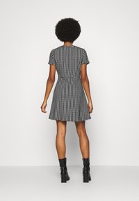 Svart och vit houndstooth klänning med kort ärm, figursydd midja och utsvängd kjol; kombinerad med svarta klumpiga klackstövlar.