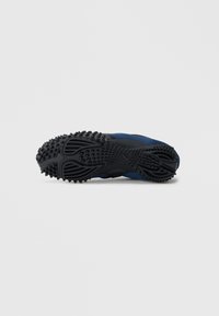 Μπλε αθλητικό παπούτσι με υφασμένο μαύρο καουτσούκ στη σόλα, που διαθέτει μοτίβο πρόσφυσης πολλαπλών κατευθύνσεων και κομψό σχεδιασμό.