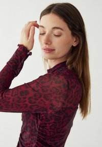 Długo-sleeve top w przezroczystym burgundowym materiale z czarnym nadrukiem w panterkę, z falbaniastymi mankietami i marszczeniami po bokach dla dodatkowej tekstury i detalu w designie.