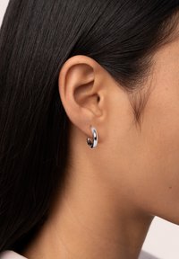 Pendientes de aro de plata con un acabado pulido, que presentan un diseño curvado y un cierre sin costuras, descansando en la oreja.