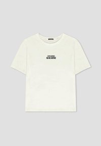 Camiseta de algodón blanca con mangas cortas y un corte holgado. Presenta la frase "CRUSHING MACHINE" impresa en negro en el centro del frente.