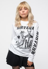 White long-sleeve shirt featuring a black graphic design with text "Nirvana" and "Incesticide." Skirt is black, pleated, and mid-thigh length.