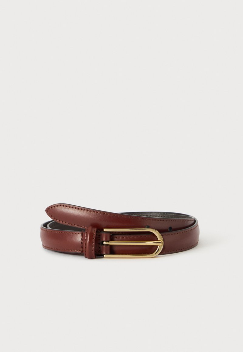 Ceinture en cuir marron roulée avec une boucle métallique de couleur or sur un fond clair uni.