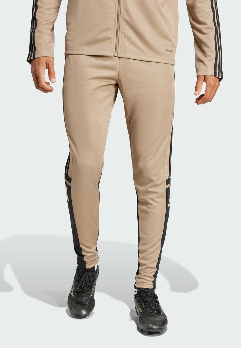 Beige sportbroek met zwarte zijkanten, slim fit ontwerp, zachte textuur en ritsdetails bij de enkels.
