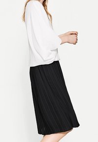 Blusa bianca, comoda e morbida con maniche a tre quarti abbinata a una gonna midi nera plissettata. Il tessuto appare leggero e текстurizzato.