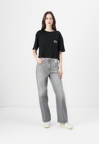 Schwarzes, kürzes T-Shirt mit einer Fronttasche; kombiniert mit hellgrauen, weiten Jeans; abgerundet mit weißen Sneakers. Einfaches Design und lässige Passform.
