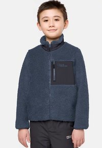 Veste polaire bleu marine foncé avec une texture douce, col montant et poche poitrine zippée. Avec logo sur la poche et matériau contrastant.