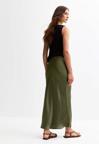 Jupe maxi satin verde olive avec une texture lisse, taille haute et fente sur le côté, associée à un haut sans manches noir et des sandales marron.