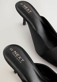 Schwarze High Heels zum Hineinschlüpfen mit glatter Oberfläche, spitzem Zehenbereich, minimalistischem Design und goldenem Logo auf der Innensohle.