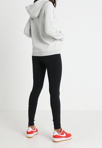 Šedá mikina s kapucí, černé legíny, červené tenisky. Důraz na ležérní styl, měkké materiály a přiléhavý střih s výraznými červenými akcenty na botách.