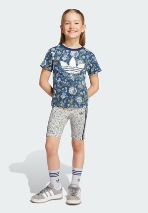 T-shirt blu con floreali e logo bianco, pantaloni corti a fantasia, scarpe grigie e calzini a righe. Maniche corte, scollatura rotonda, design aderente.