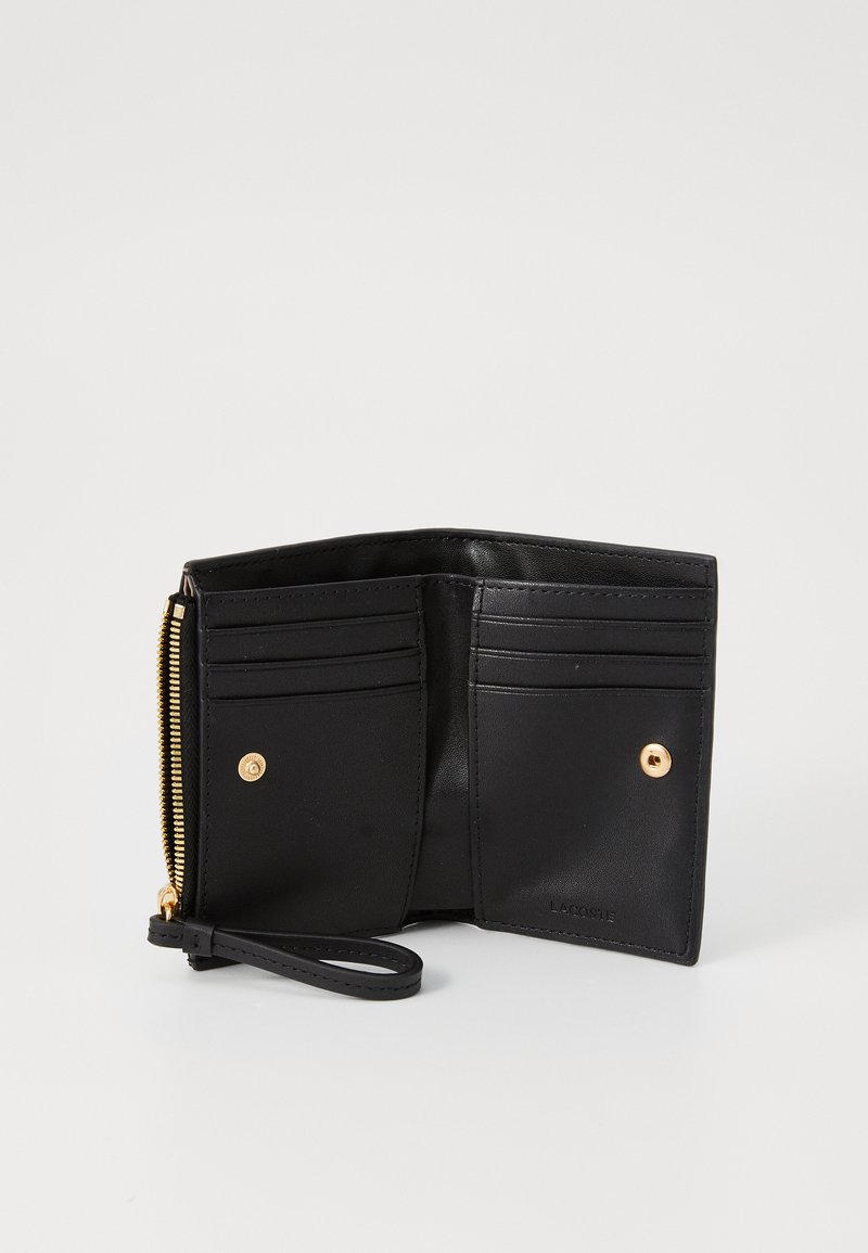 Portefeuille en cuir noir avec fermeture éclair, doté de plusieurs emplacements pour cartes, d'un bouton pression et d'une dragonne. Texture lisse et design minimaliste.