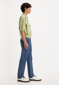 Roheline ja kreemjas triibuline lühikeste varrukatega särk, sinised denim teksad ja valged kingad mustade paeltega, toodud küljelt.