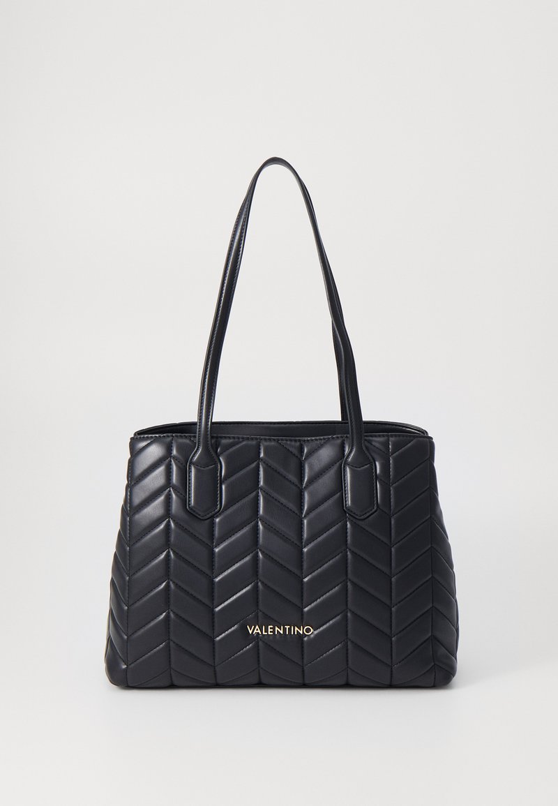 Bolso tote negro acolchado con un patrón de espiga, textura suave y asas dobles. Nombre de la marca en dorado en la parte frontal.
