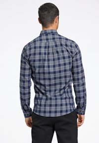 Camisa a cuadros en tonos azul marino y gris, confeccionada en tejido de sarga, con mangas largas, botones en los puños y un detalle en el yugo trasero.