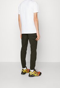 Biała bawełniana koszulka, oliwkowe spodnie cargo z bocznymi kieszeniami oraz czarno-żółto-pomarańczowe buty sportowe z siateczkowym i gumowym wzorem.