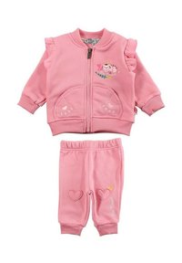 Survêtement en polaire rose comprenant une veste à fermeture éclair avec des manches à volants et des poches en forme d'empreintes de pattes, associé à un pantalon à taille élastique avec des accents en forme de cœur.