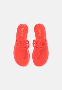 Röda plastflip-flops med en klipp-ut logotyprem och en platt sula. Insidan har guldtexten "LAUREN RALPH LAUREN."