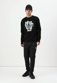 Svart sweatshirt med 3D-texten "KARL LAGERFELD" och svarta byxor i hundtandsmönster. Bärs med en svart keps och svarta sneakers.