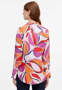Langærmet bluse i silkeagtigt stof med et farverigt abstrakt bladmønster i pink, orange og rød, med en buet kant og knapmanchetter.