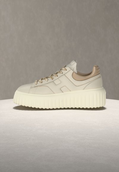 Kremasto bežna usnjena superga z debelim rebrastim podplatom, bež oblazinjenim petnim delom in ujemajočimi vezalkami na nevtralni površini in ozadju.