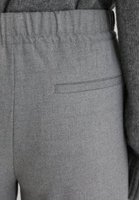 Zbliżenie na szare materiałowe spodnie z elastycznym pasem i jedną poziomą kieszenią z tyłu, noszone z ciemnoszarym swetrem.