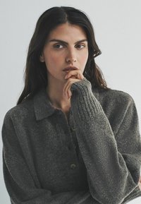 Sivý pletený sveter s golierom, s detailmi gombíkov, rebrovanými manžetami a textúrovanou tkaninou. Mäk materiál strednej váhy.