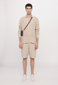 Camisa de linho bege com botões, mangas arregaçadas, combinada com calções a condizer. Ténis brancos e uma pequena mala de tiracolo completam o visual.