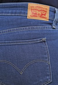 Jeans de mezclilla azul con un parche de cuero etiquetado "Levi Strauss & Co." y una costura curva distintiva en el bolsillo trasero.