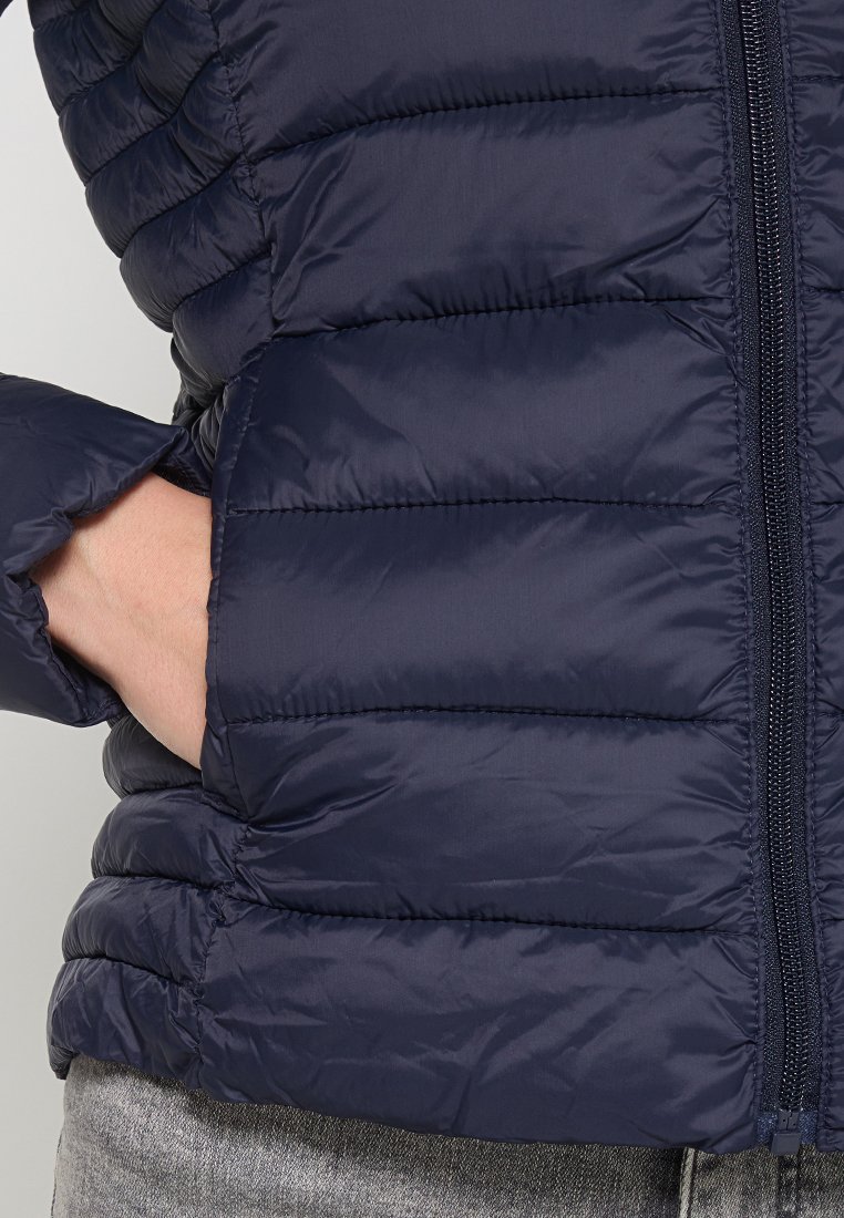 Giacca puffer trapuntata blu navy con zip frontale, design a cuciture orizzontali e polsini elasticizzati. Presenta una tasca laterale per le mani.