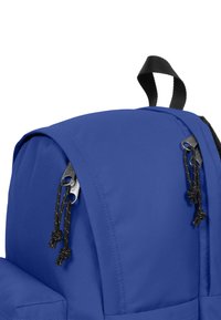 Modrá batoh s texturovanou tkaninou, vybavený černými zipovými táhly a pletenými šňůrkami. Obsahuje horní držadlo na nošení a tvarované popruhy na ramena.