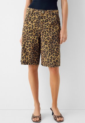 Femme portant un short imprimé léopard mi-long avec poches latérales, assorti à des sandales à talons imprimé léopard et un haut noir.