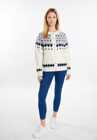 Pletený cardigan v krémové barvě s šedou horní částí, zdobený geometrickými vzory v námořnické modři. Zapínání na knoflíky a ribbovanými manžetami, zkombinovaný s modrými džíny.