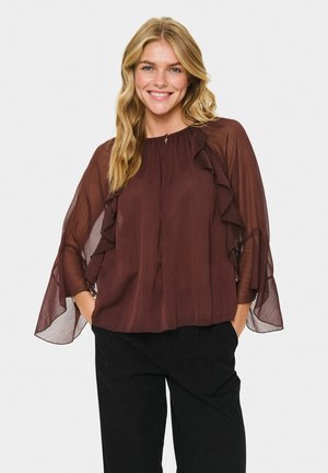 Maroon blouse with ruffled detailing, lightweight sheer sleeves, and a gathered neckline, paired with black wide-leg trousers.