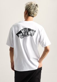 White cotton t-shirt featuring a large black graphic with the text “VANS ‘OFF THE WALL’” and skateboard design on the back.