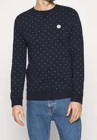Sudadera de algodón azul marino con un pequeño patrón en toda la prenda de formas verde claro, cuello redondo y puños y dobladillo acanalados.