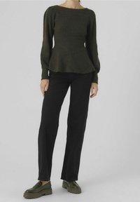 Dunkelgrüner Strickpullover mit langen Ärmeln und einem Peplum-Design, kombiniert mit schwarzen, hochtaillierten Hosen und dunkelgrünen Plateauslippern.