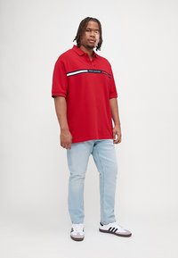 Rød polo skjorte med korte ærmer, har et vandret stribet design i blå og hvid, parret med lyseblå jeans og hvide sneakers.
