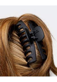 Schwarze Kunststoff-Haarspange, die braunes Haar zusammenhält. Die Spange hat ein breitgezahntes Design und einen sicheren Verschlussmechanismus.