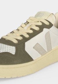 Χαμηλό sneaker με πράσινες σουέντ επικαλύψεις, λευκές δερμάτινες επιφάνειες, μπεζ κορδόνια και ανοιχτό μπεζ λαστιχένια σόλα.