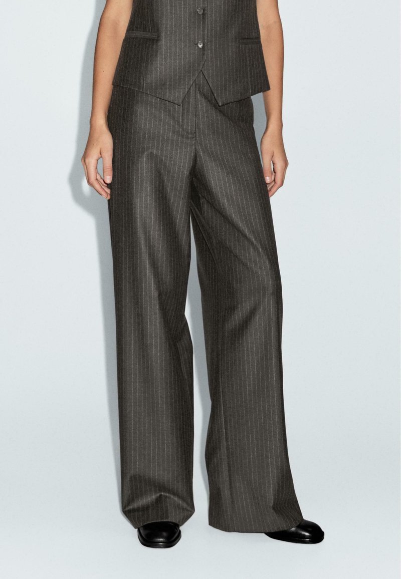Pantaloni da completo grigio a righe con design a gamba larga, in tessuto sartoriale e con una texture sottile. Abbinati a scarpe con tacco nere.