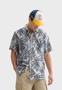 Košeľa s krátkym rukávom modrej farby s listovým vzorom, s gombíkmi a vreckom na prsiach. Doplnkovaná modro-žltou čiapkou.