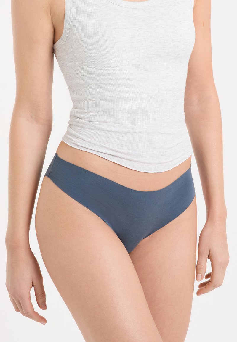 Ropa interior de algodón azul con textura suave, diseño de talle bajo y bordes sin costuras. Estilizada con una camiseta ajustada gris sin mangas.