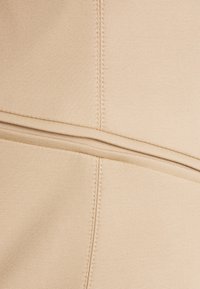 Tissu beige avec une texture lisse, présentant des coutures visibles et un détail de couture horizontale. Le matériau semble durable et flexible.