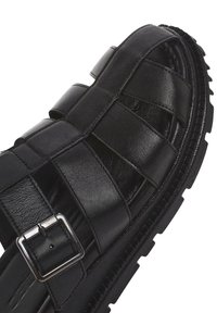 Sandal in pelle nera con design intrecciato, fissata con una fibbia argentata e una suola in gomma testurizzata per una migliore aderenza.