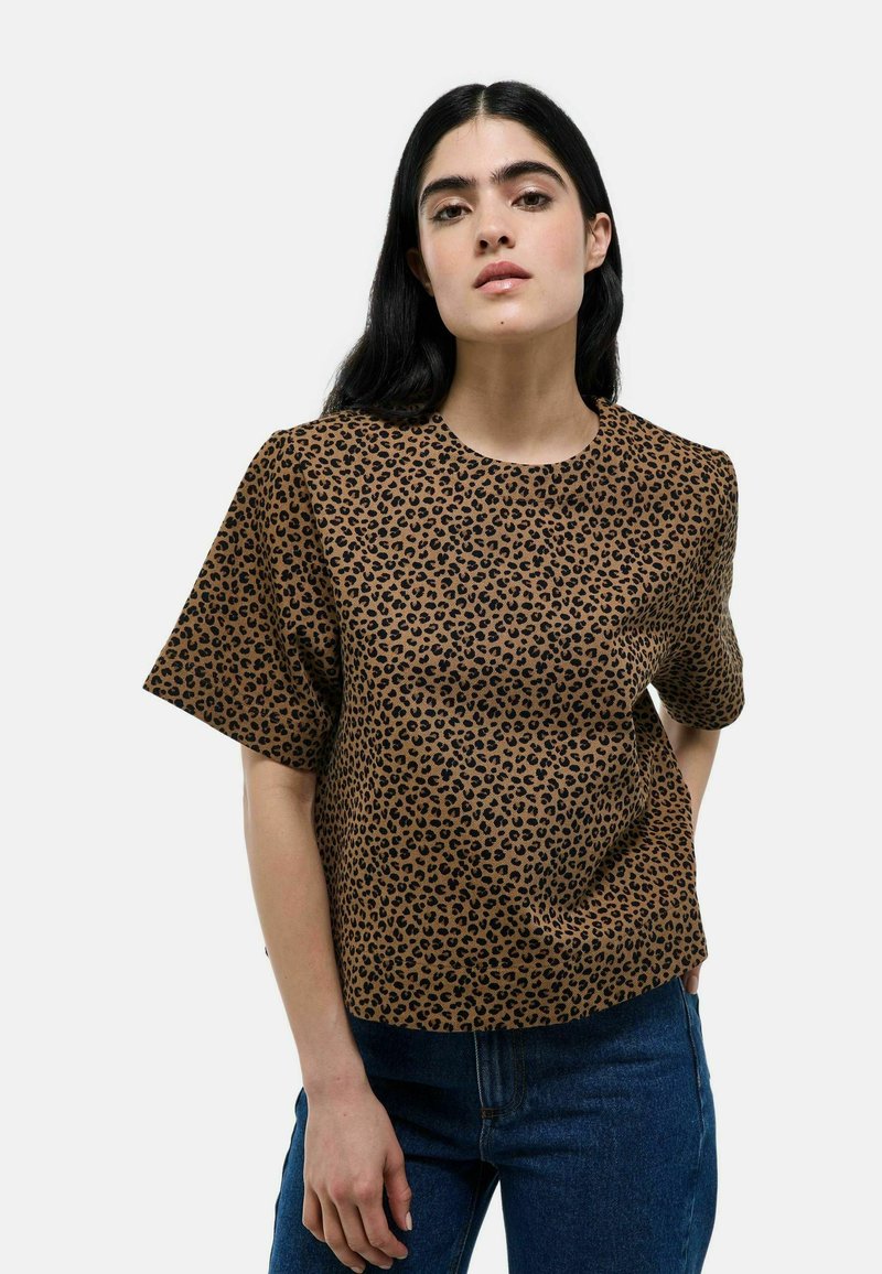 Haut à manches courtes en imprimé léopard marron, fabriqué en tissu texturé. Encolure ronde et coupe décontractée, associé à un jean en denim bleu.
